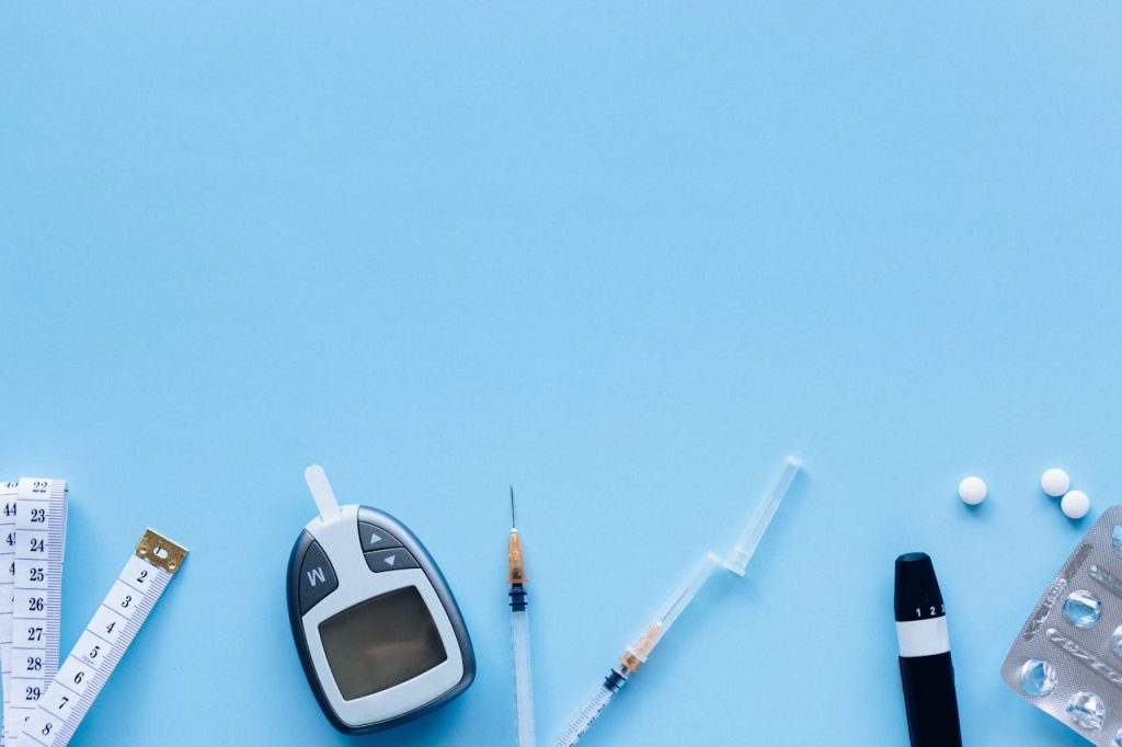 pexels-photo-6941883 Flat lay of diabetes management tools including glucose meter, syringe, and pills on blue background.